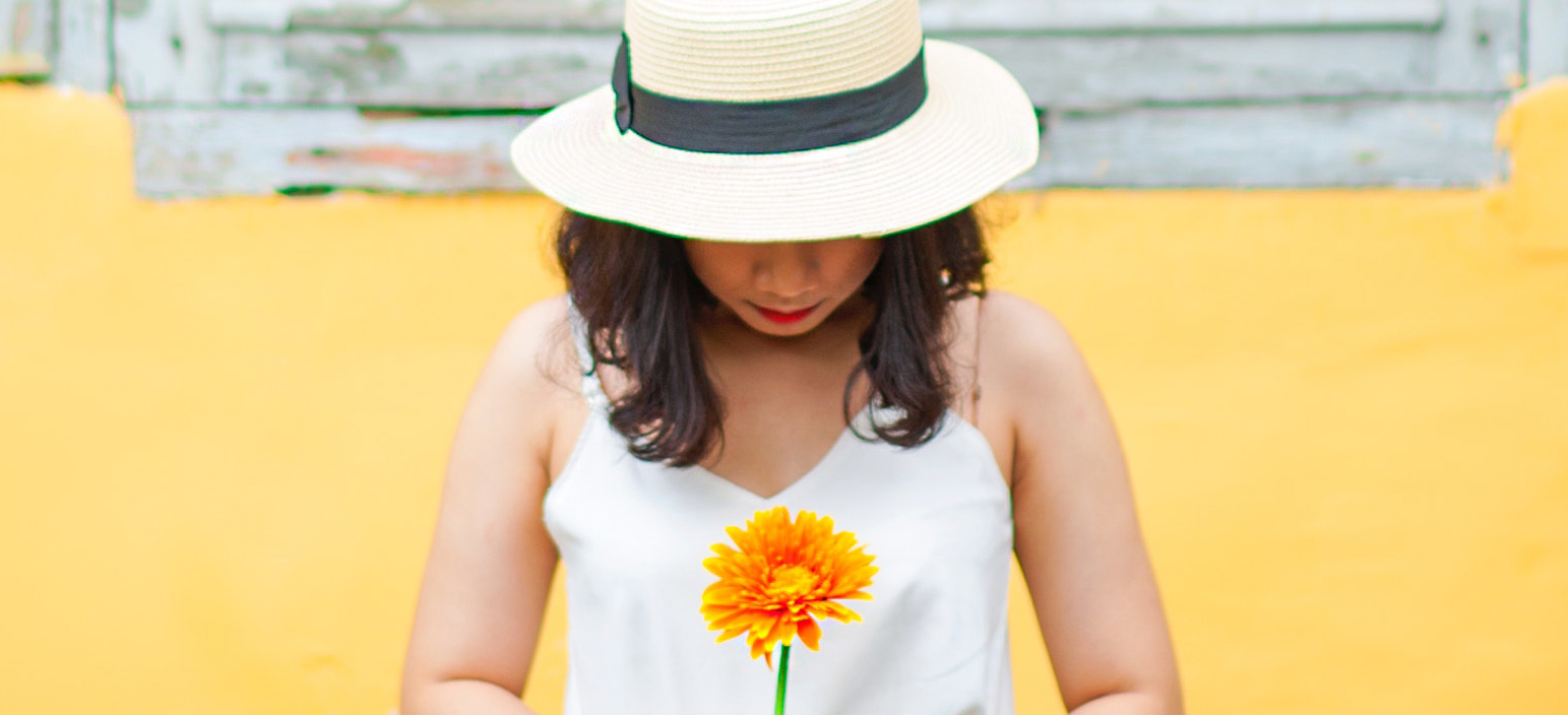 A young person in a hat holds a yellow flower